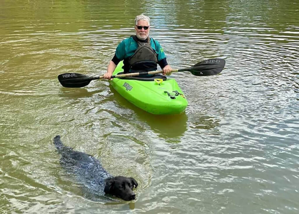 man kayaking beside swimming dog
